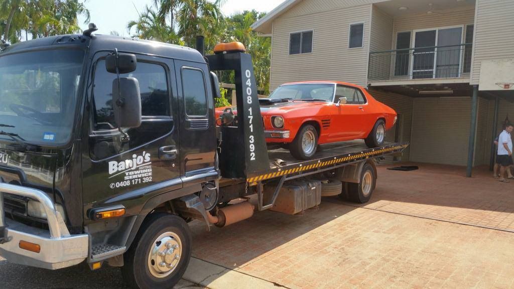 Black Tow Truck Carrying an Orange Classic Car in Front of a Two-story House — Banjo's Anytime Towing in Berrimah, NT