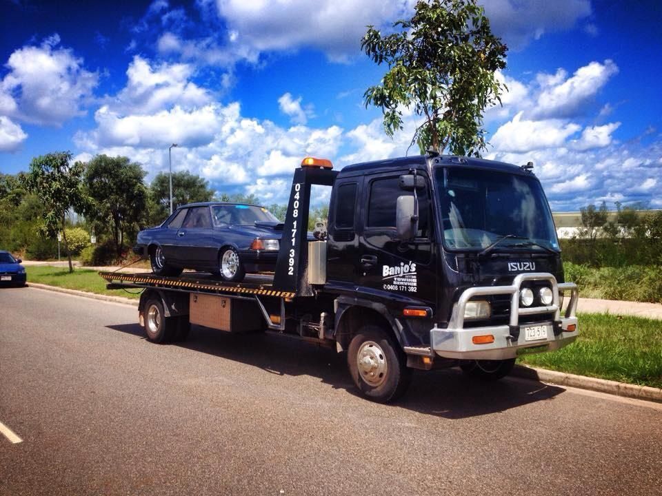 Black tow truck carrying a blue classic car on a sunny day — Banjo's Anytime Towing in Humpty Doo, NT