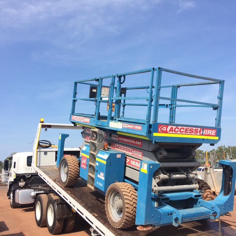 Blue scissor lift on a flatbed truck, under a blue sky. The lift has an access hire label — Banjo's Anytime Towing in Humpty Doo, NT