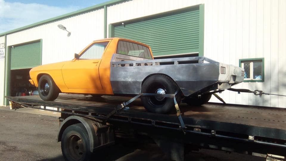 Orange and grey pickup truck on a flatbed tow truck in front of a building with green doors — Banjo's Anytime Towing in Humpty Doo, NT