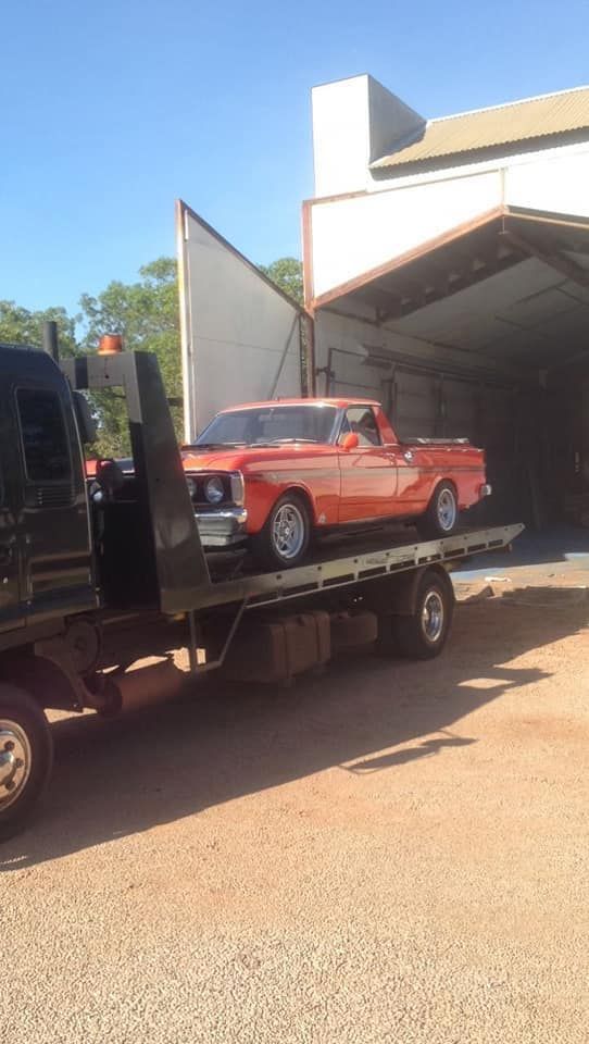 Orange vintage car on a flatbed truck in front of a building with open doors 