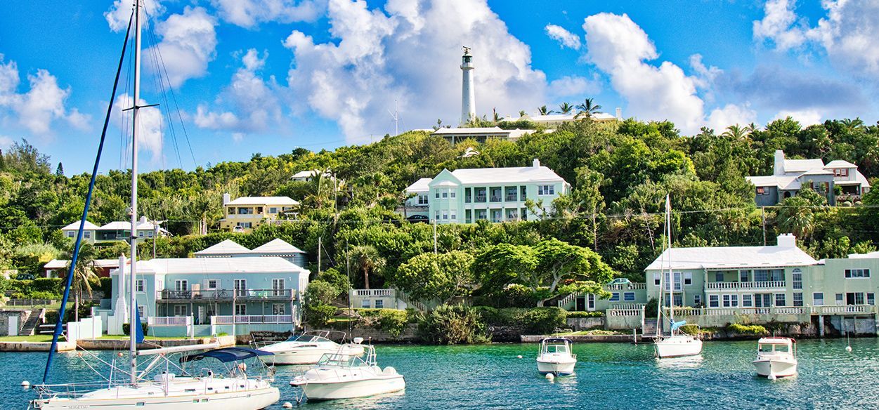 A group of boats are docked in a harbor with a lighthouse in the background.