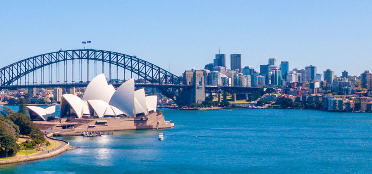The sydney harbor bridge and the opera house are visible in this panoramic view of sydney.