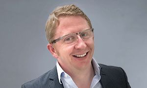 A man wearing glasses and a suit is smiling for the camera.