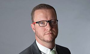 A man wearing glasses and a suit and tie is looking at the camera.