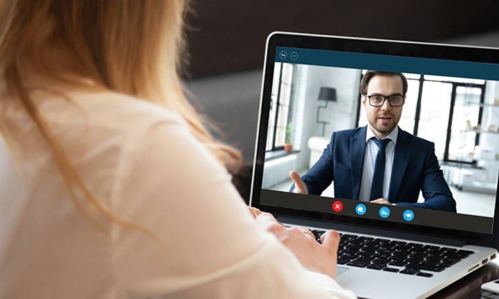 A woman is sitting in front of a laptop computer having a video call with a man in a suit.