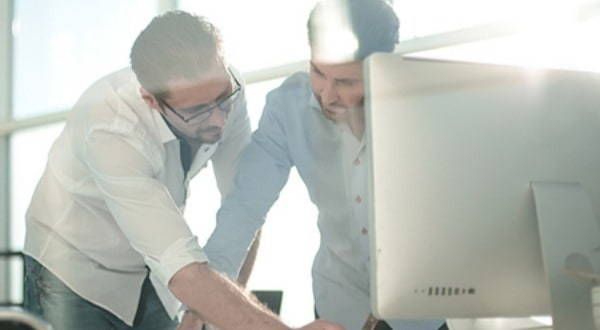 Two men are looking at a computer screen together.
