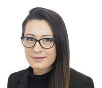 A woman wearing glasses and a black jacket is smiling for the camera.
