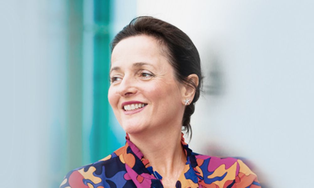A woman in a colorful shirt is smiling and looking to the side.