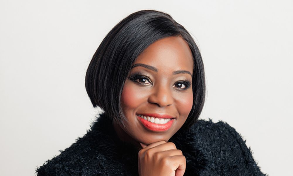A woman wearing a black fur coat and red lipstick is smiling.