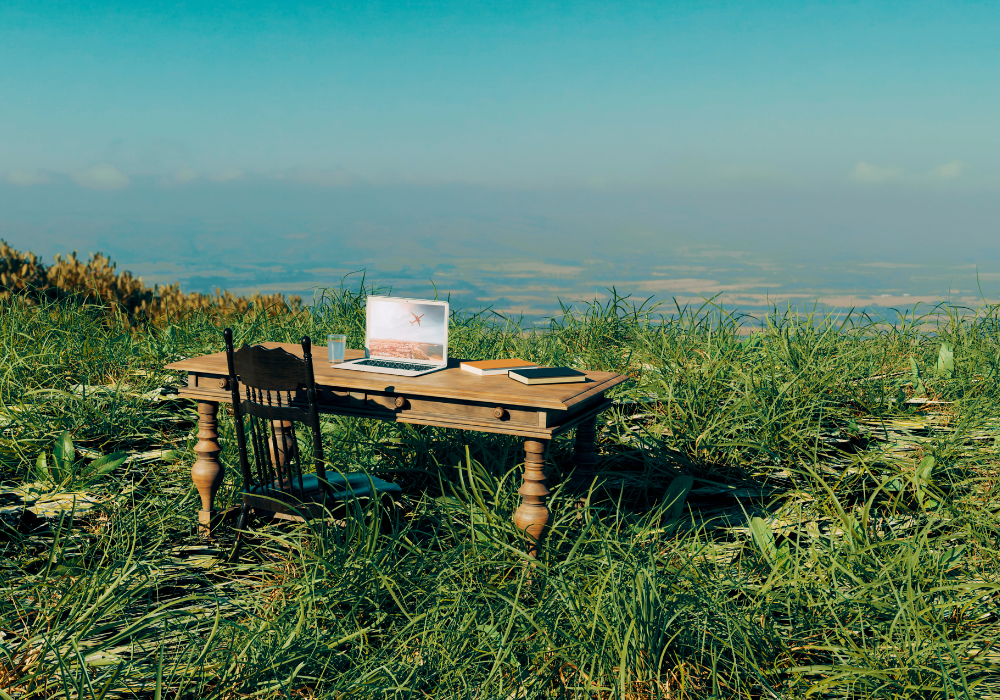A wooden table with a laptop on it in the middle of a grassy field.