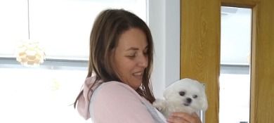 A woman is holding a small white dog in her arms.