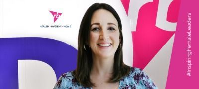 A woman is smiling in front of a pink and blue background.