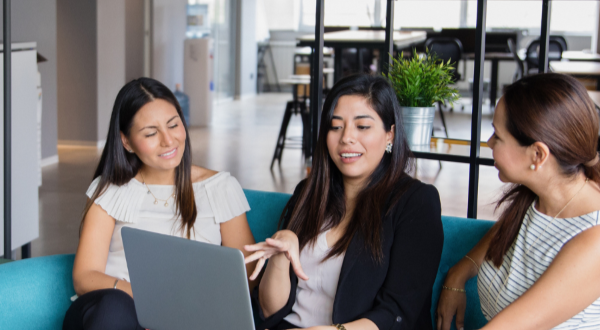 Three women are sitting on a couch looking at a laptop computer.