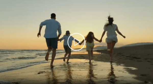 A family is running on the beach holding hands.