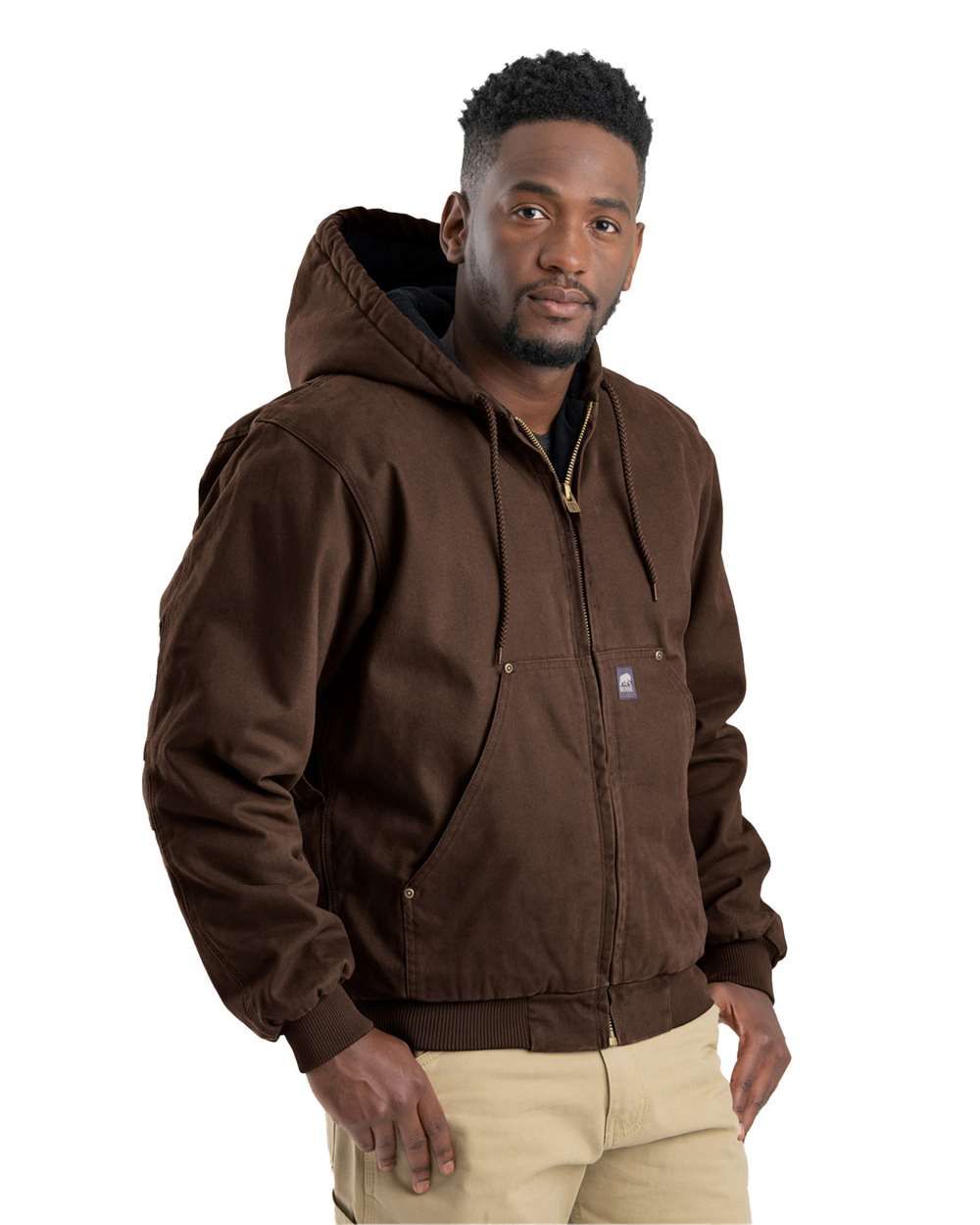 Man in a green hooded jacket and khaki pants smiling; standing, indoors.