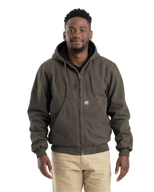 Man in a green hooded jacket and khaki pants smiling; standing, indoors.