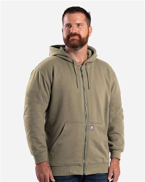 Man in a green zip-up hoodie with a beard, in a studio setting.