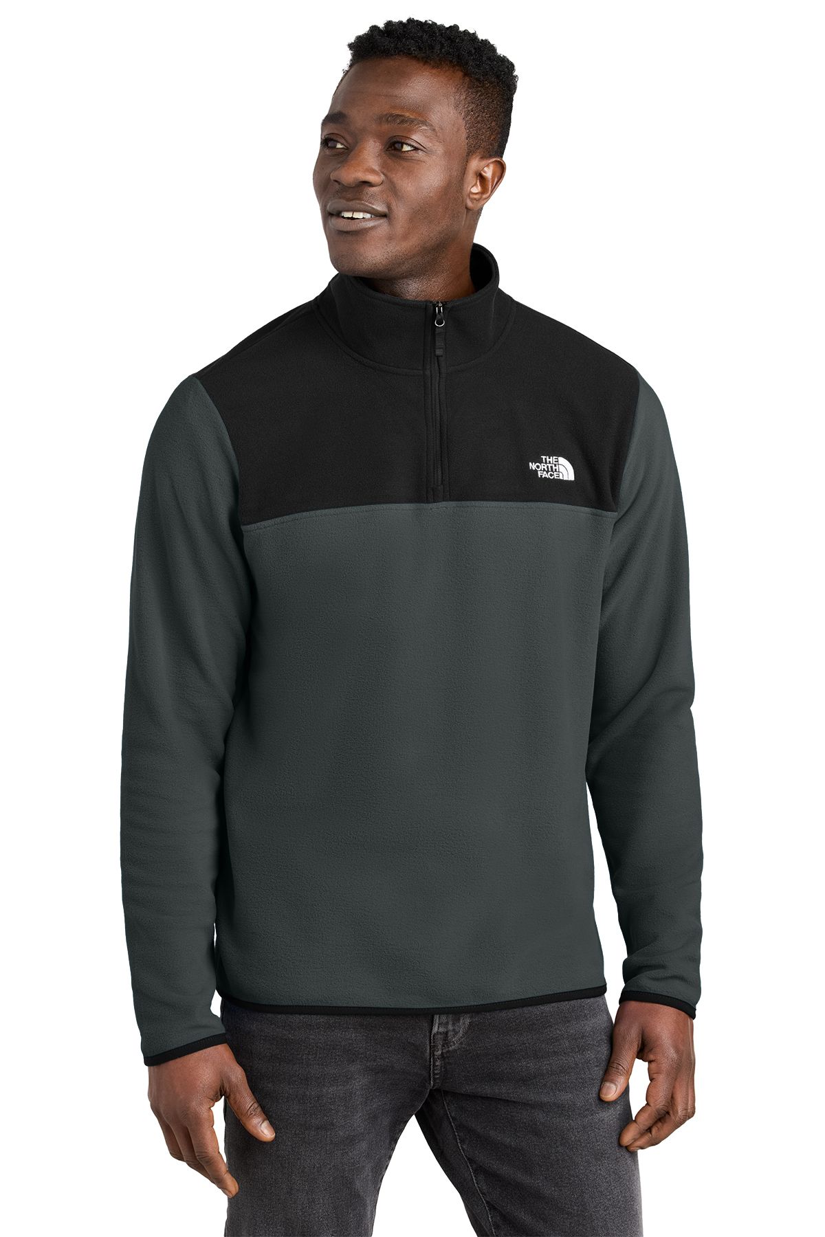 Man in a black and green fleece pullover, smiling, standing, indoors.