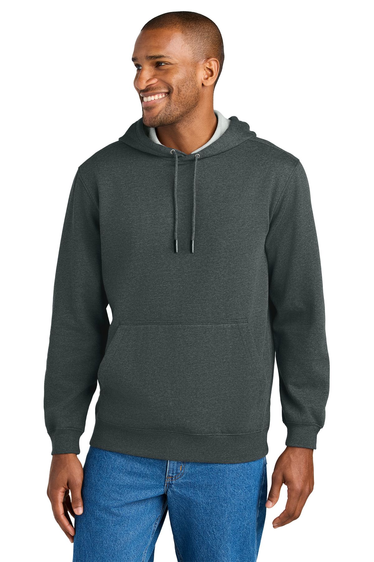 Man wearing a gray hooded sweatshirt and blue jeans smiles, standing indoors.