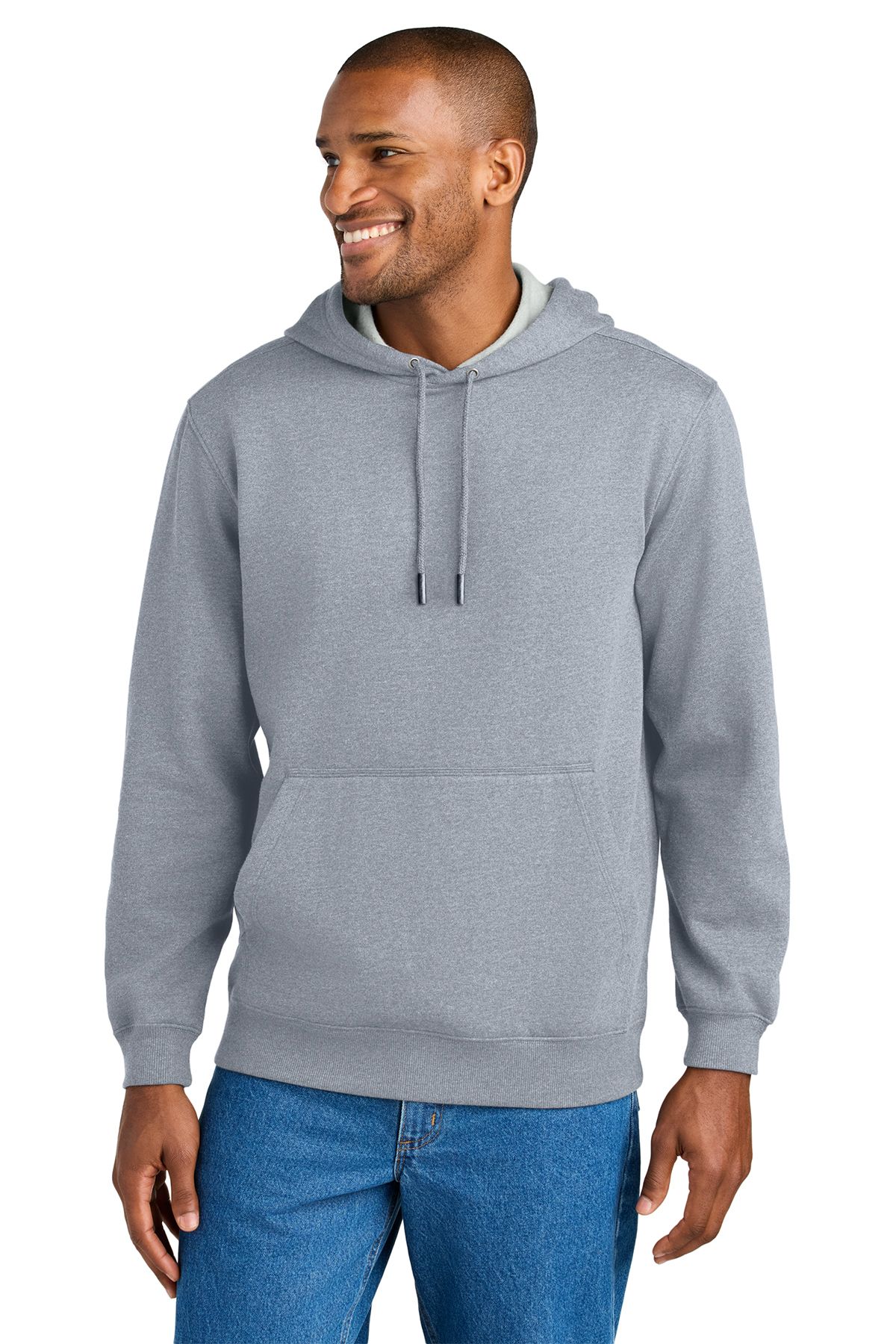 Man wearing a gray hooded sweatshirt and blue jeans smiles, standing indoors.