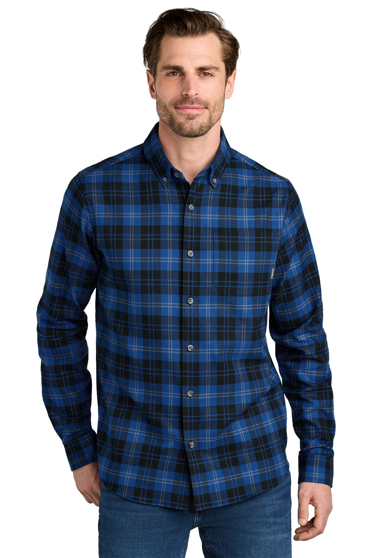 Man wearing blue and black plaid shirt, buttoned at the collar, over blue jeans; standing, smiling.