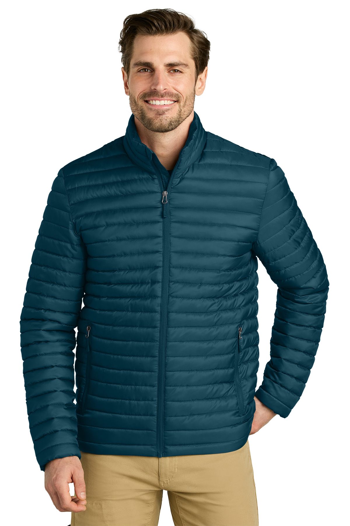 Man wearing a teal puffer jacket, smiling. Stands in front of a white background, wearing khaki pants.