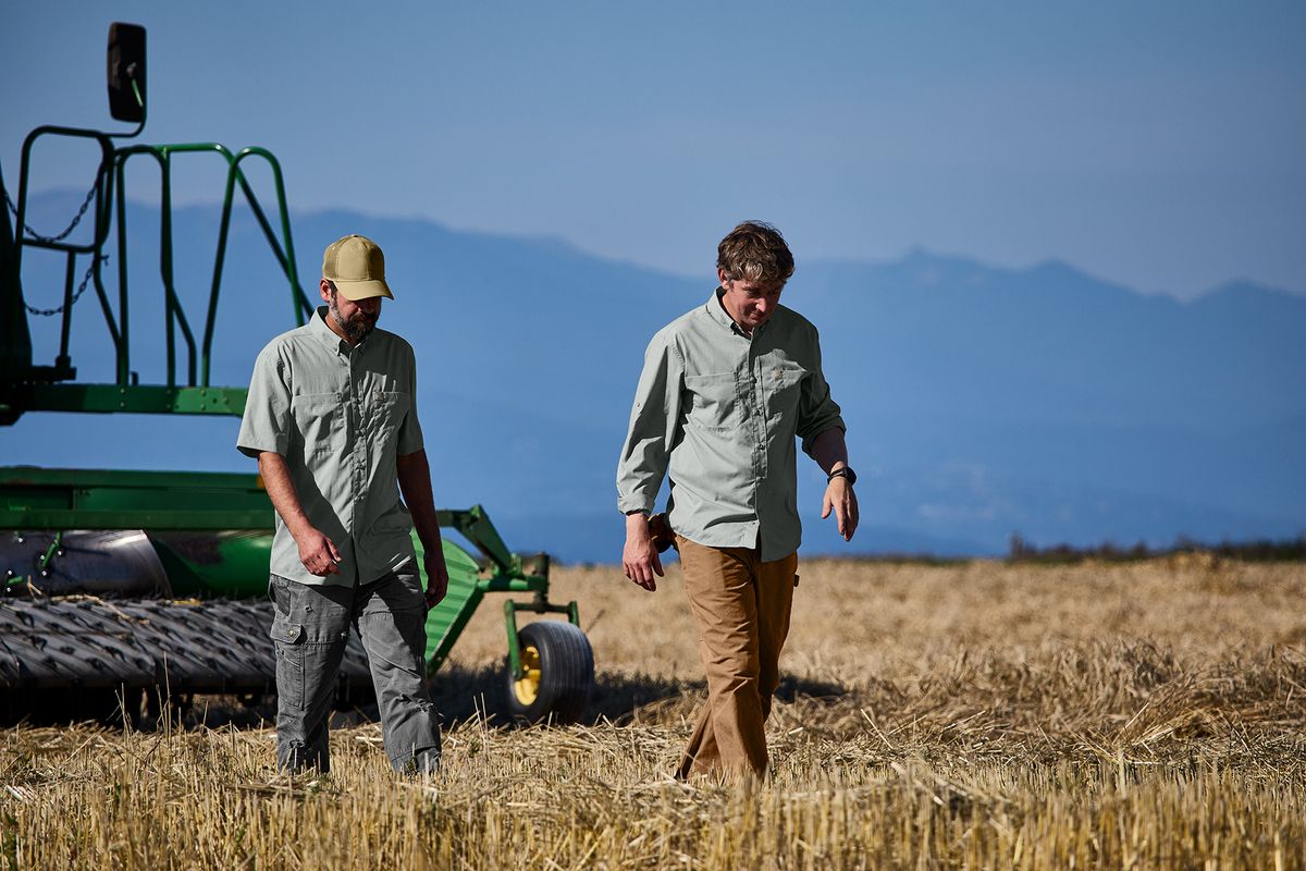 Two man walking in a field in front of a tractor wearing our button-down short-sleeve work shirts by Carhartt