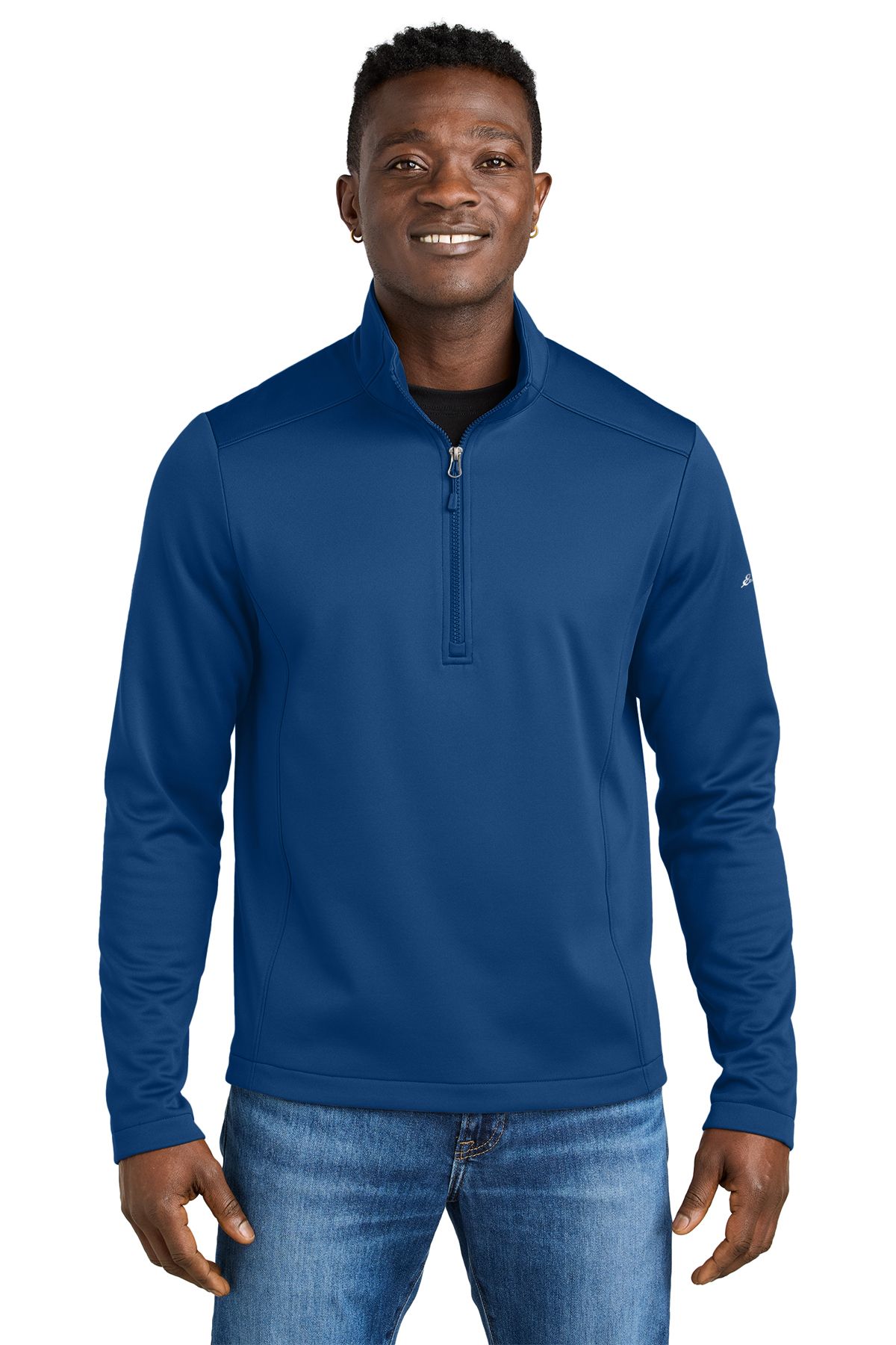 Man in navy blue quarter-zip top and jeans, smiling.