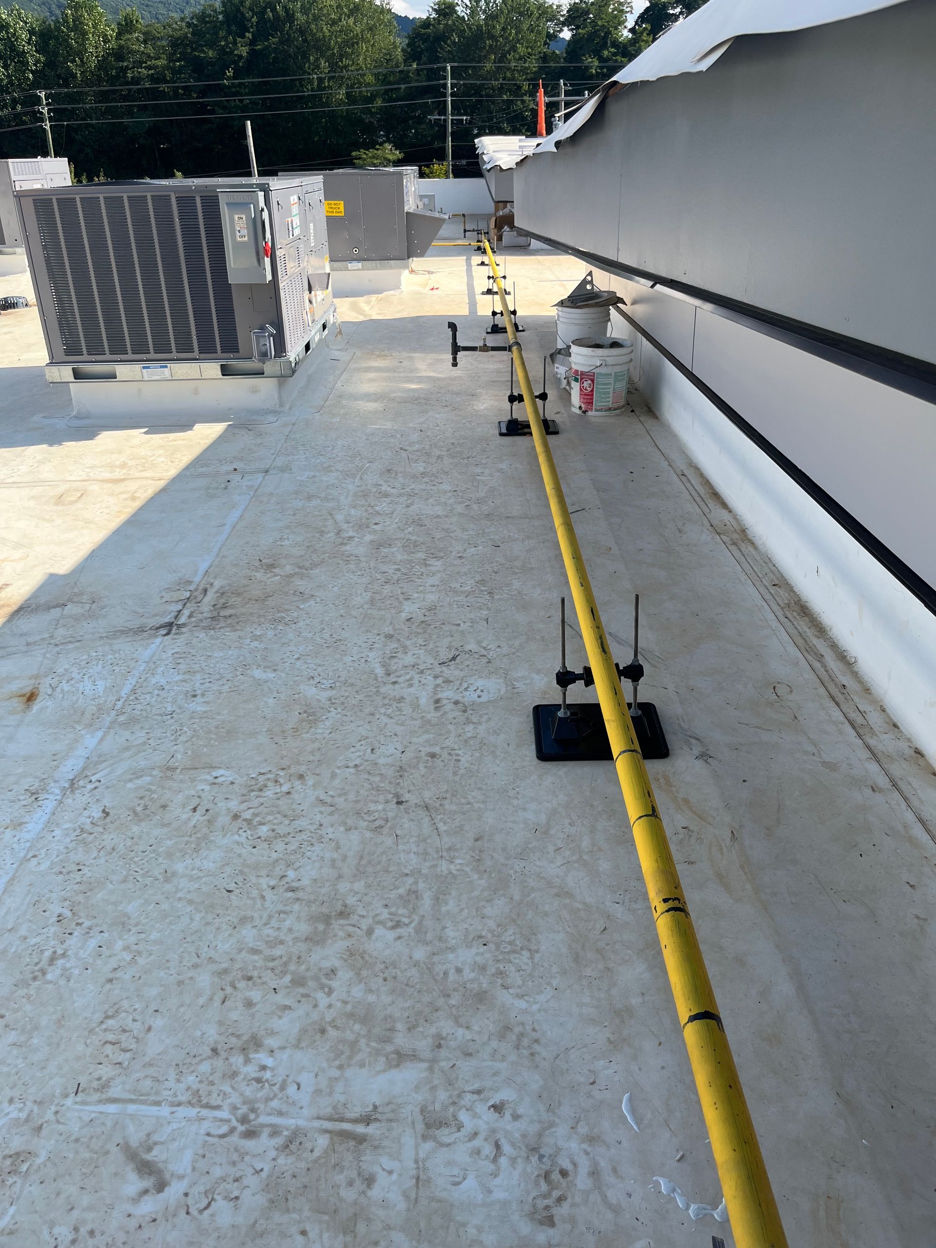 Industrial plumbing pipes suspended by metal rods from a corrugated metal ceiling and brown steel beam.