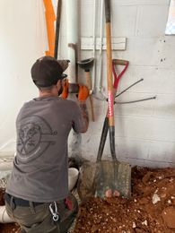 MRJ Plumbing replacing copper and cast iron drain lines. A dug up basement floor with shovels and dirt as well as a plumber making the repair.