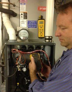 Technician inspecting wiring inside an open appliance with a yellow tool in a workshop setting