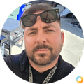Man taking a selfie outdoors, wearing sunglasses on his head and a lanyard.