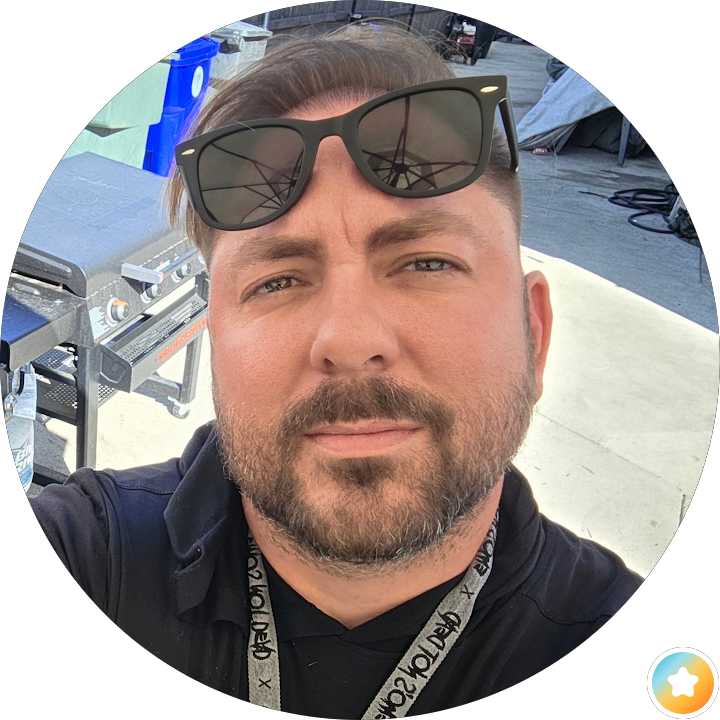 Man taking a selfie outdoors, wearing sunglasses on his head and a lanyard.
