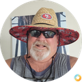 Man wearing a red San Francisco 49ers sun hat, black sunglasses, and a sleeveless gray shirt, smiling indoors
