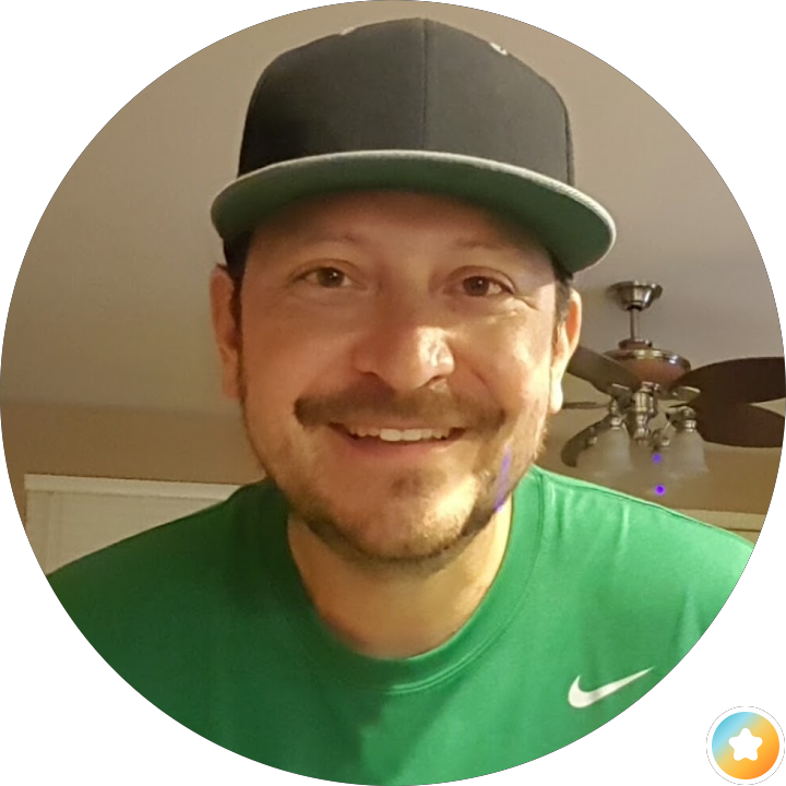 Smiling man in a black cap and green shirt indoors, with a ceiling fan in the background