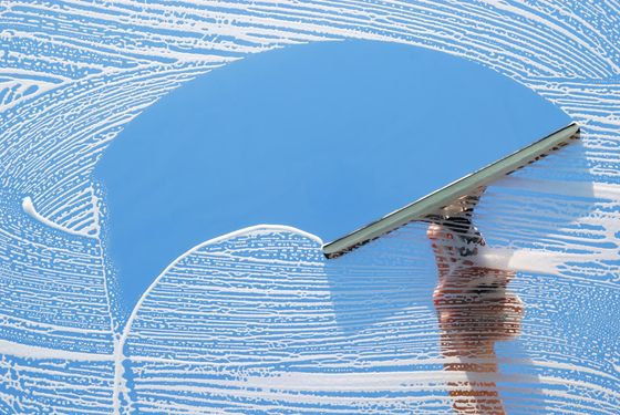Hand using a squeegee to clean white suds from a blue windowpane