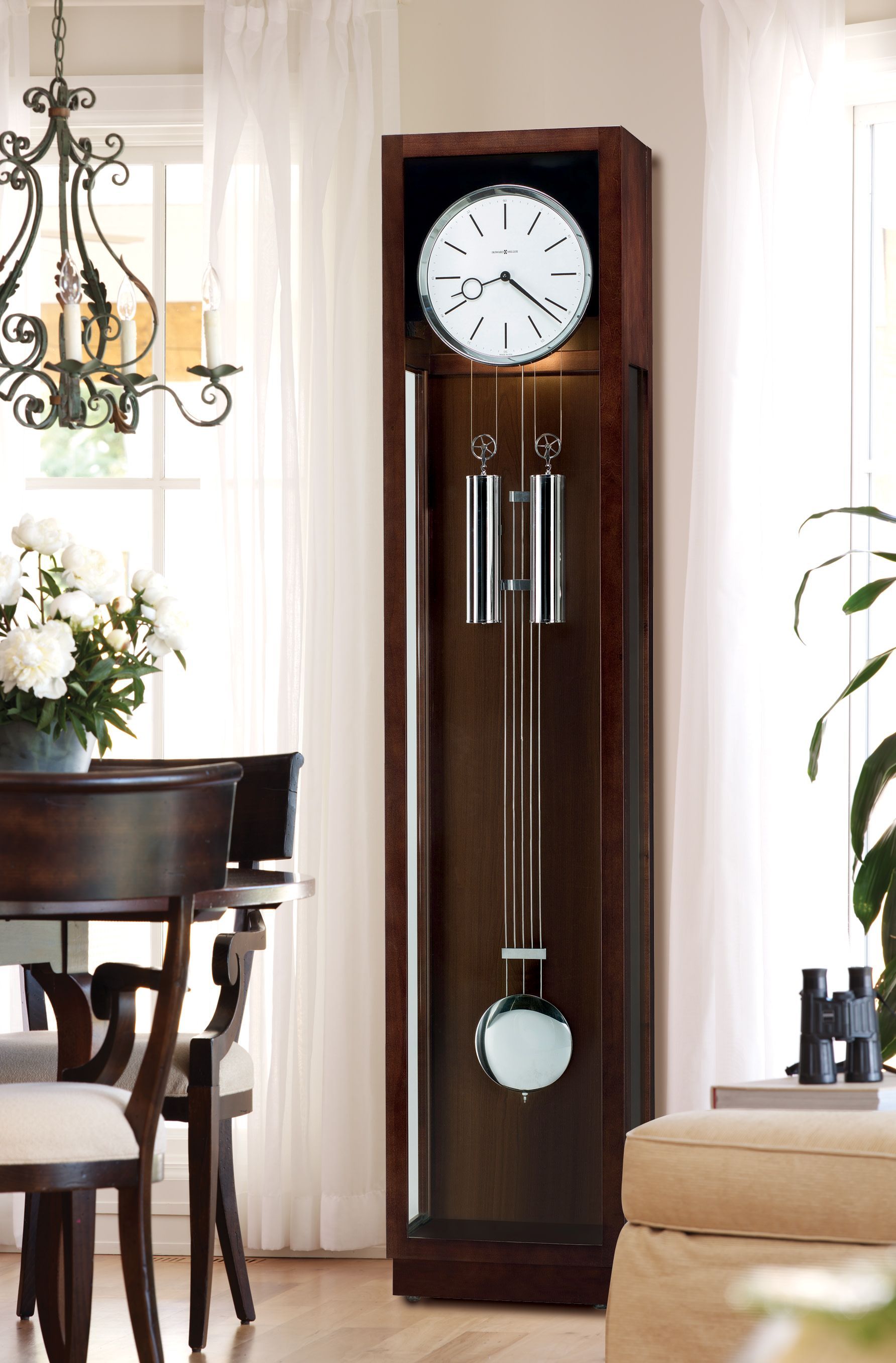 A large grandfather clock in a living room with a table and chairs