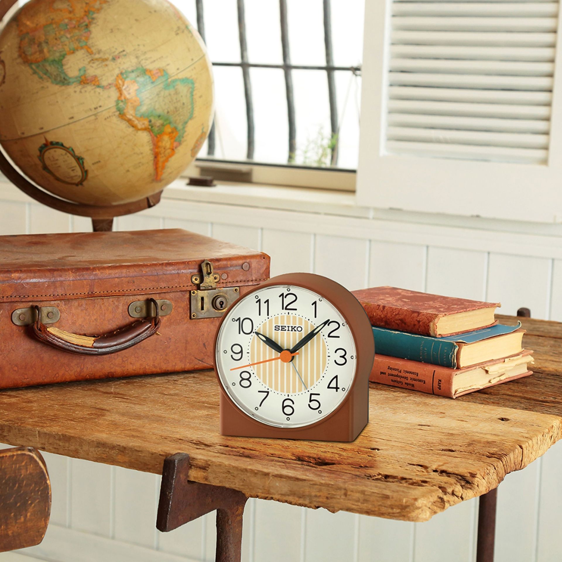 A clock sitting on a wooden table next to a suitcase and a globe