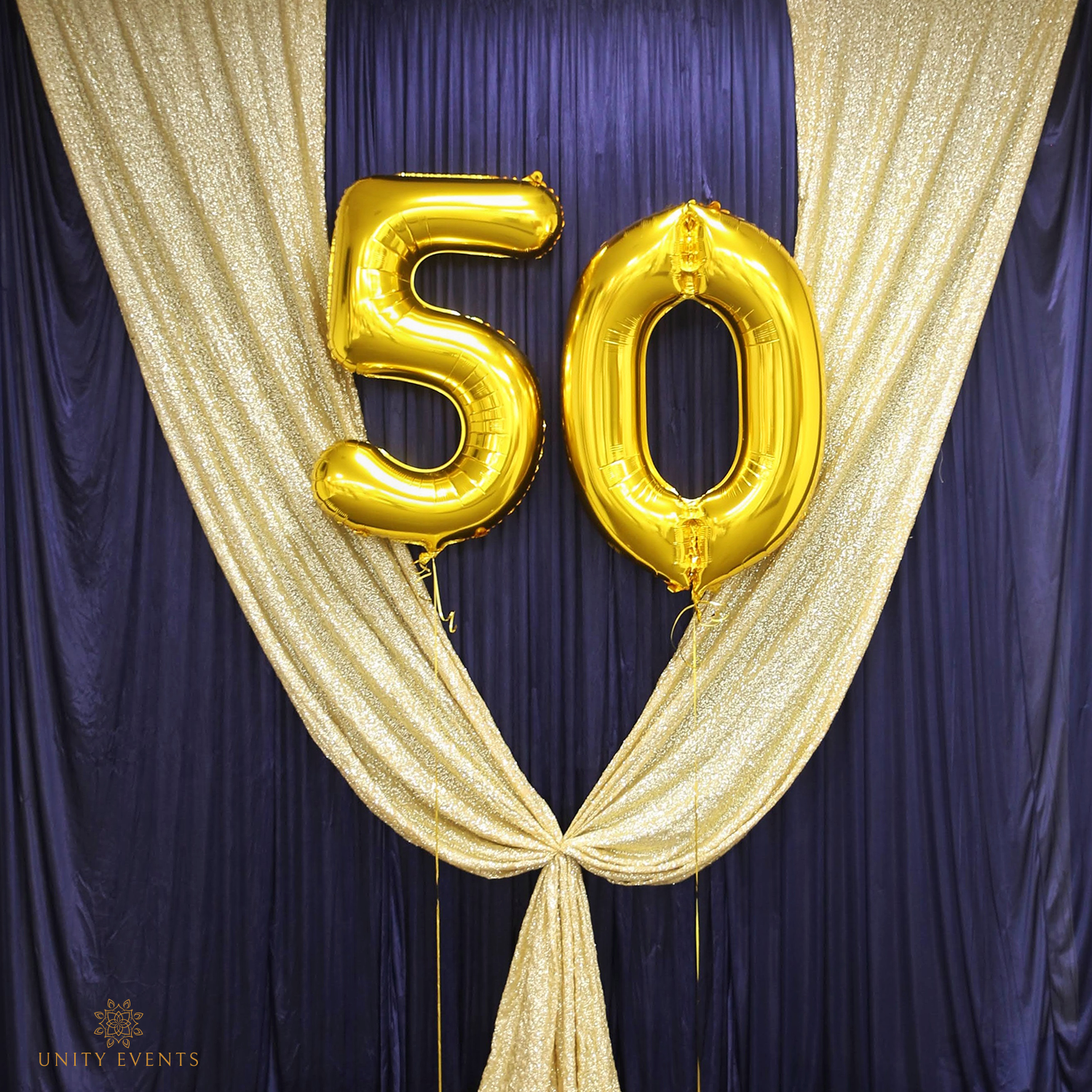 Gold “50” balloons against purple and gold draped backdrop with event decor