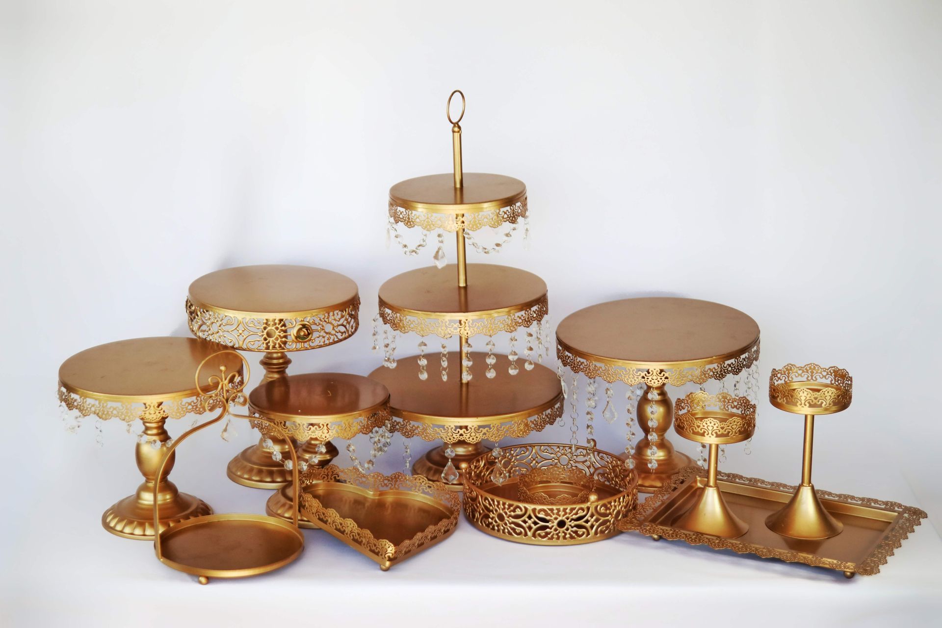 Gold dessert stands and trays with ornate cake displays on a white background