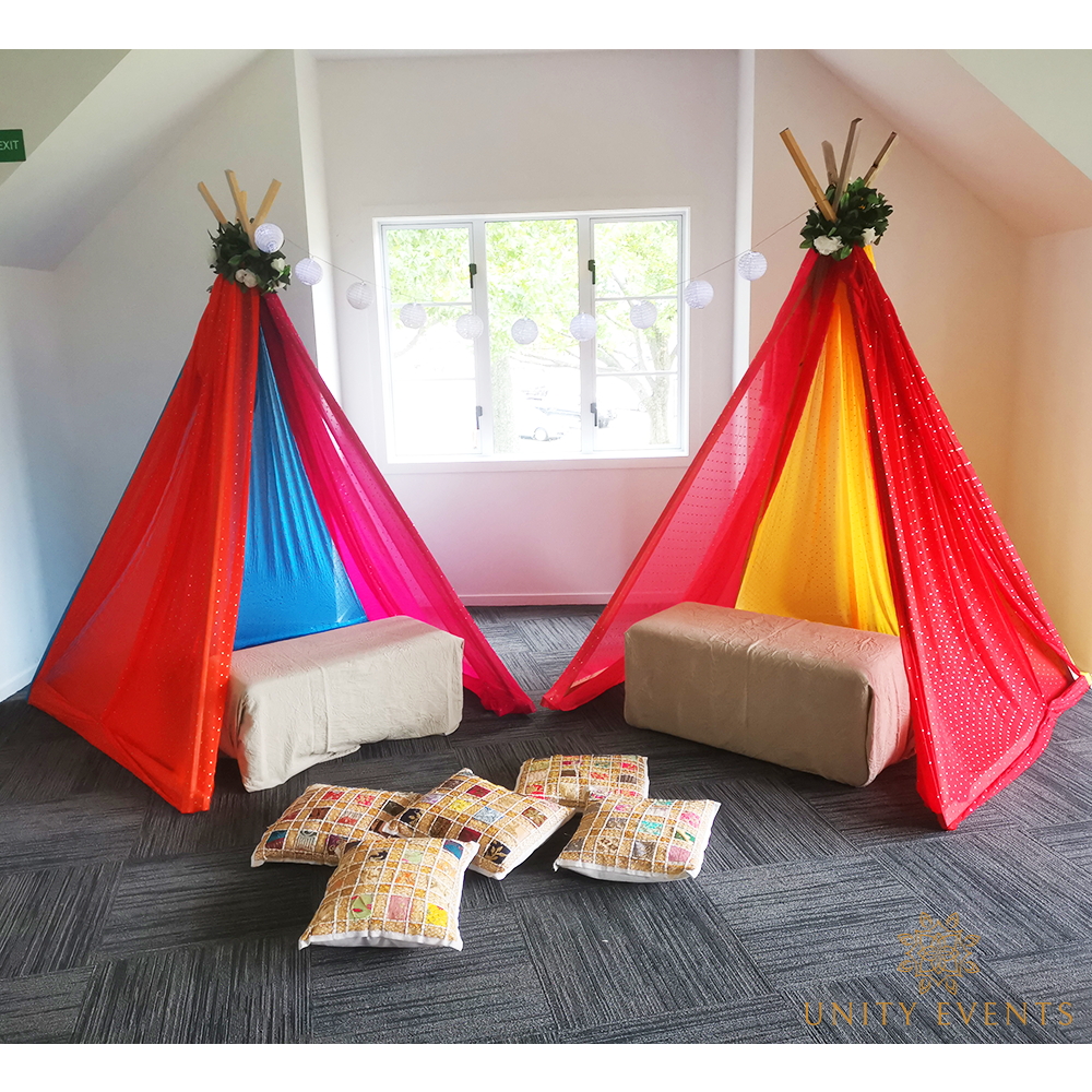 Two colorful teepee tents with cushions and pillows in a bright indoor playroom