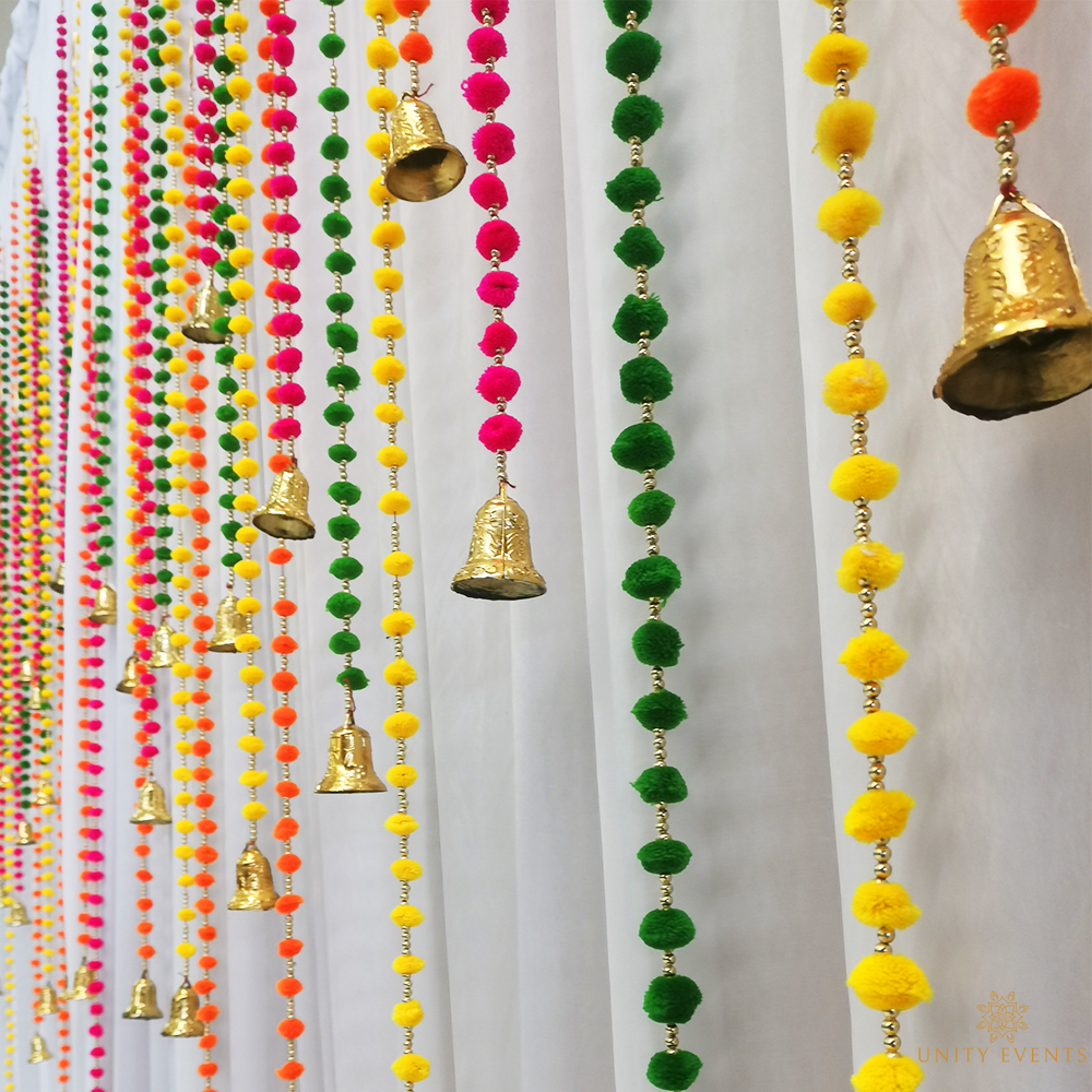 Colorful hanging garlands and gold bells decorating a white wall
