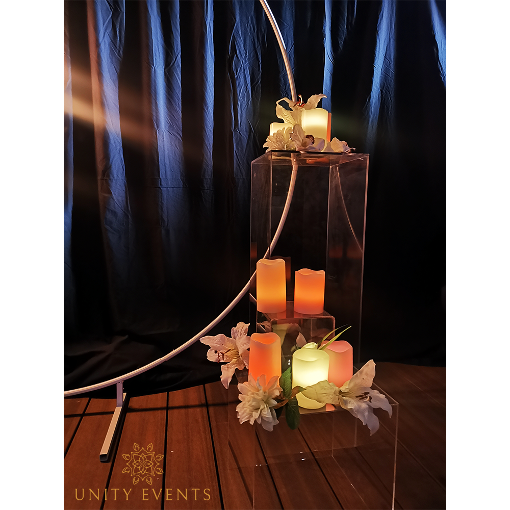 Elegant candlelit event décor with glowing orange candles, white flowers, and dark drapery on a wooden floor