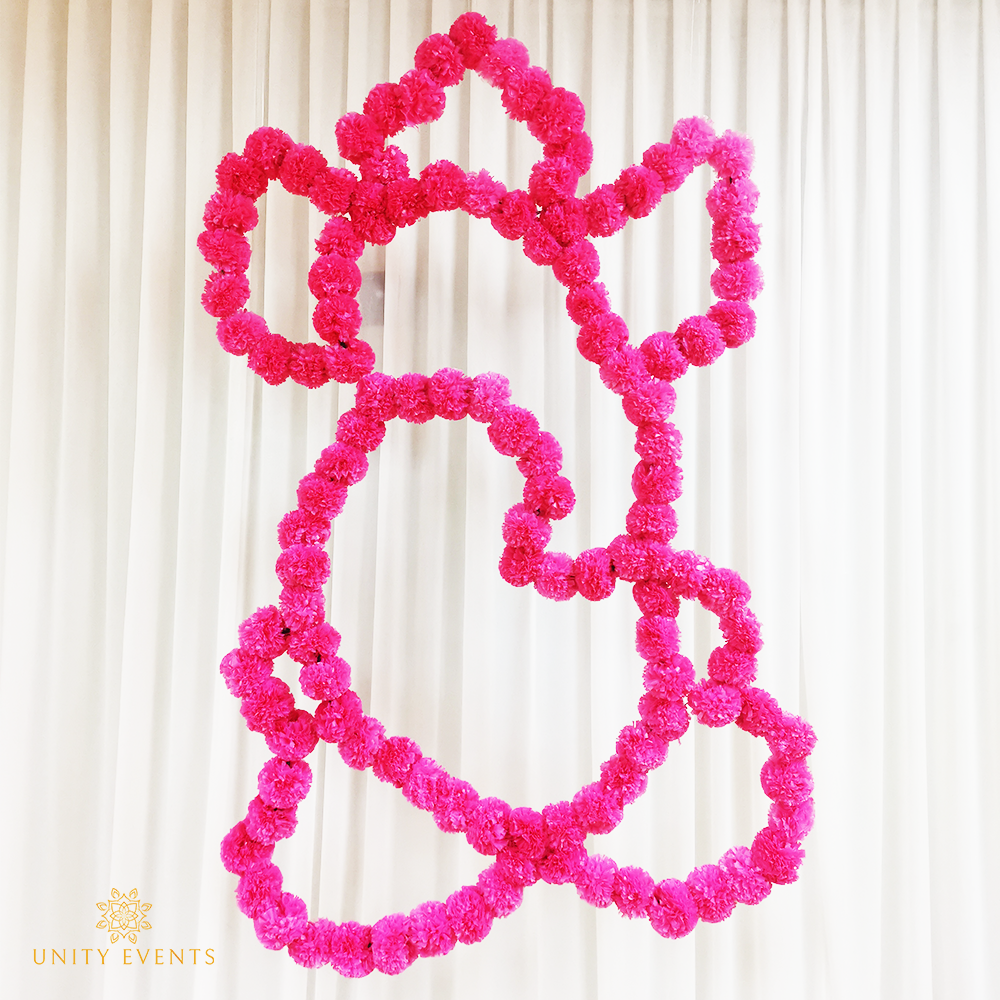 Pink flower garland arranged into an abstract looping shape on a white curtain backdrop
