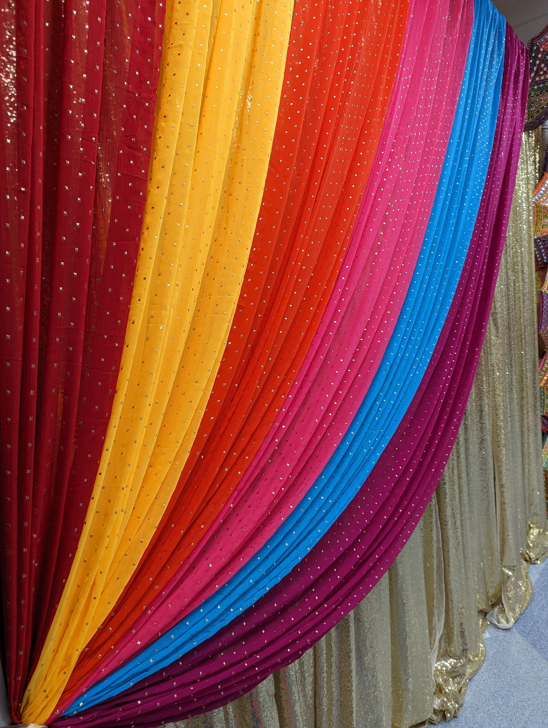 Colorful draped fabric backdrop with vertical stripes in red, orange, yellow, magenta, blue, and silver
