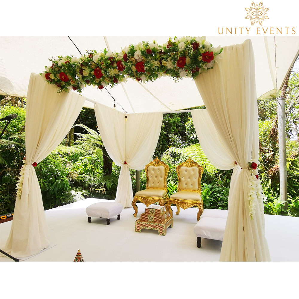 Elegant white wedding canopy with cream drapes, floral garland, and gold chairs on an outdoor patio