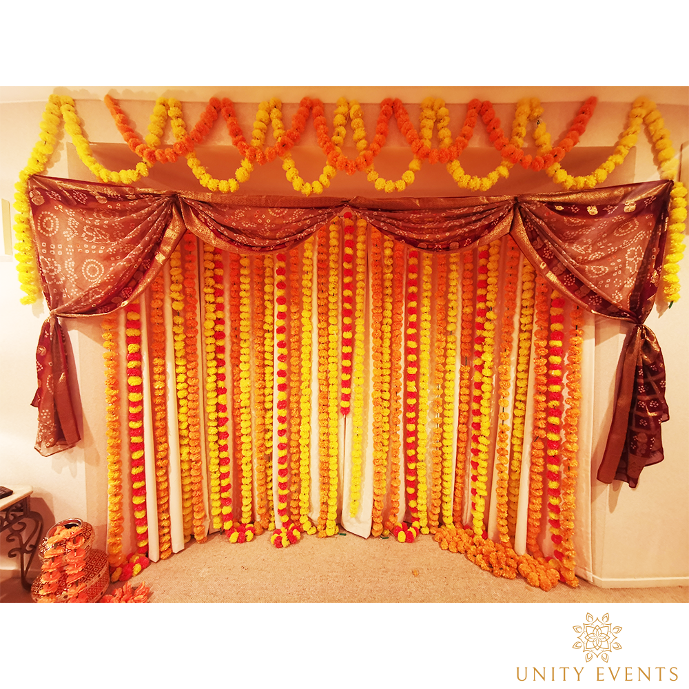 Marigold and maroon draped event backdrop with floral garlands and curtains