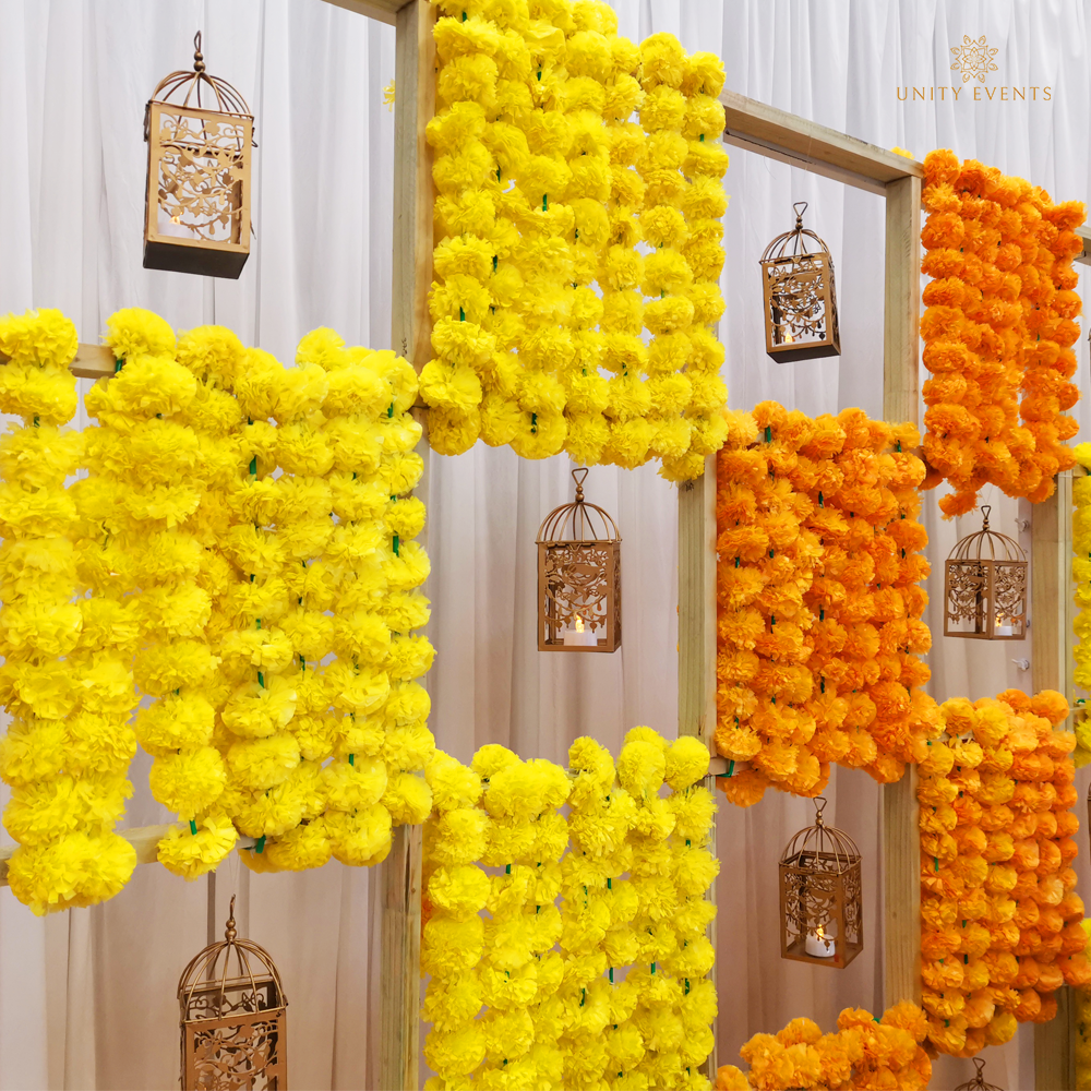 Yellow and orange marigold garlands and lanterns hanging on a decorative wall backdrop