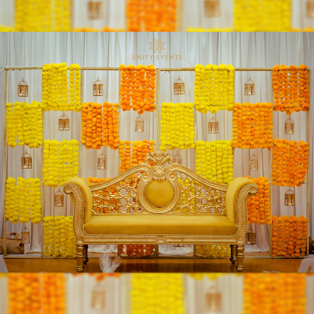 Gold ornate sofa before yellow and orange floral wall panels, likely a decorative event stage backdrop